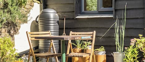 A rustic outdoor seating area with a wooden table and chairs, surrounded by potted plants and a large water tank.