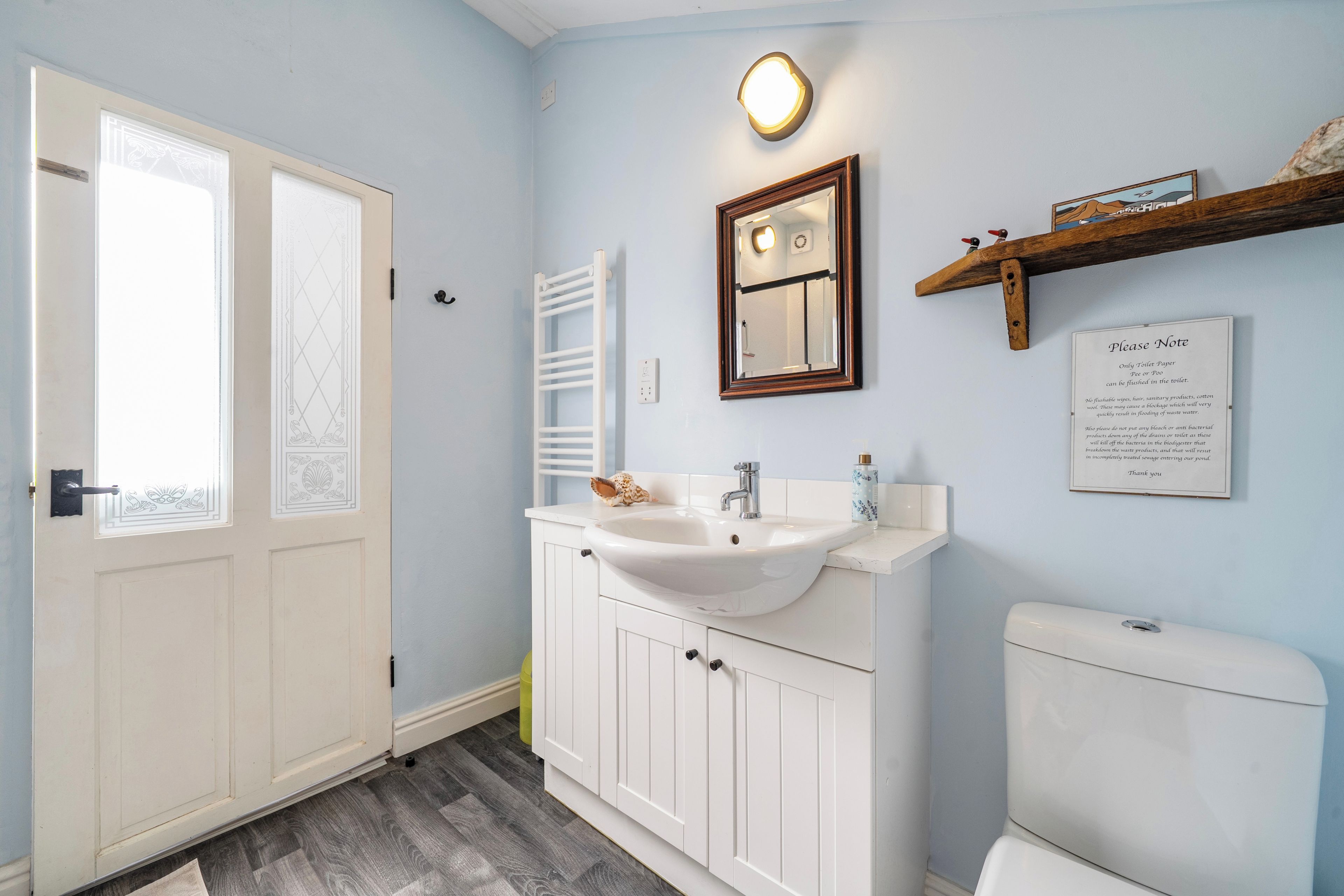 A bathroom with a white sink, mirror, and toilet. There is a sign on the wall with instructions.