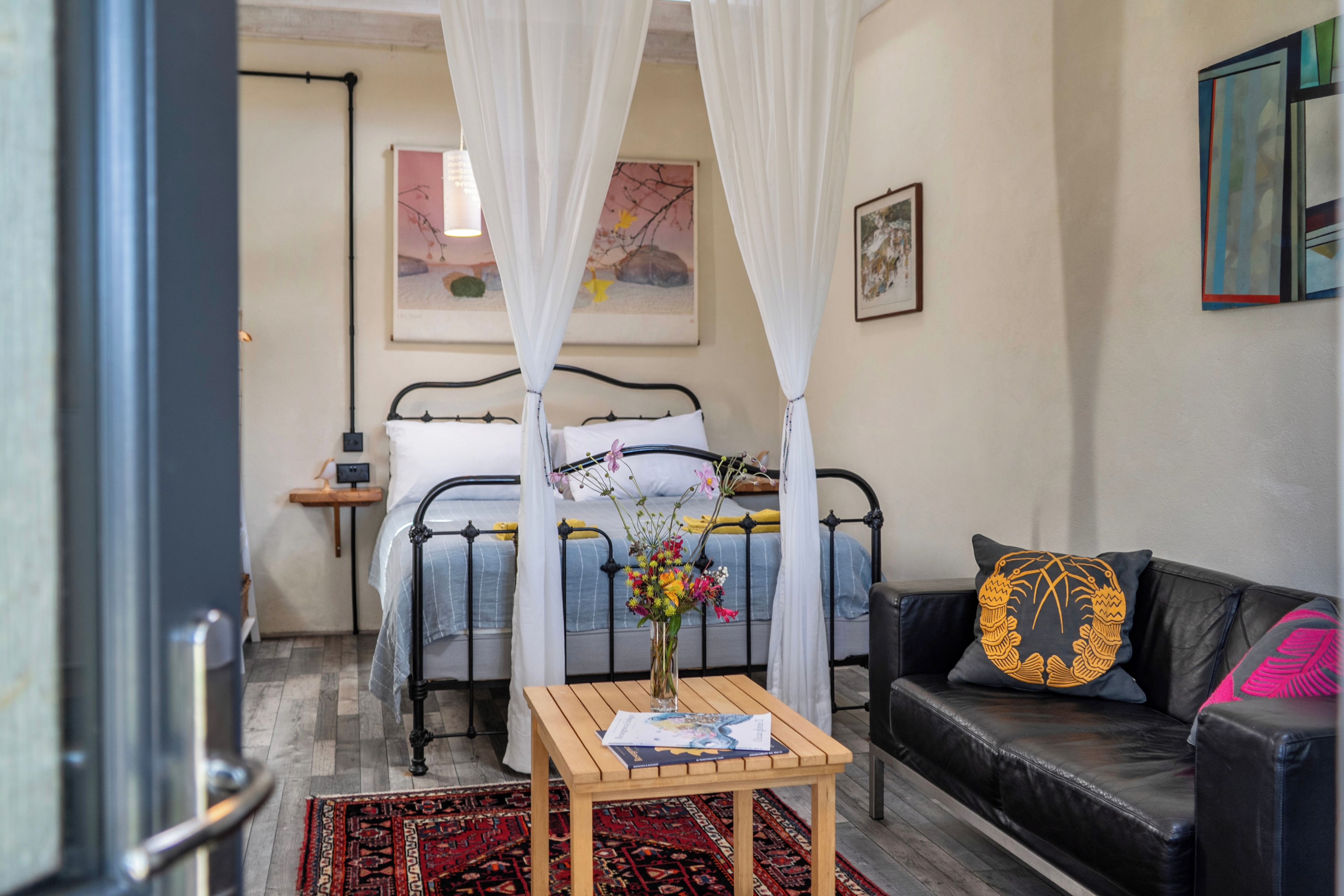 A bedroom with a bed, a bedside table with a book, a couch, and a decorative pillow.