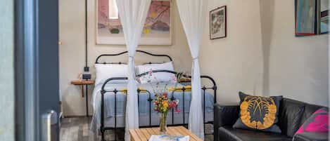 A bedroom with a bed, a bedside table with a book, a couch, and a decorative pillow.