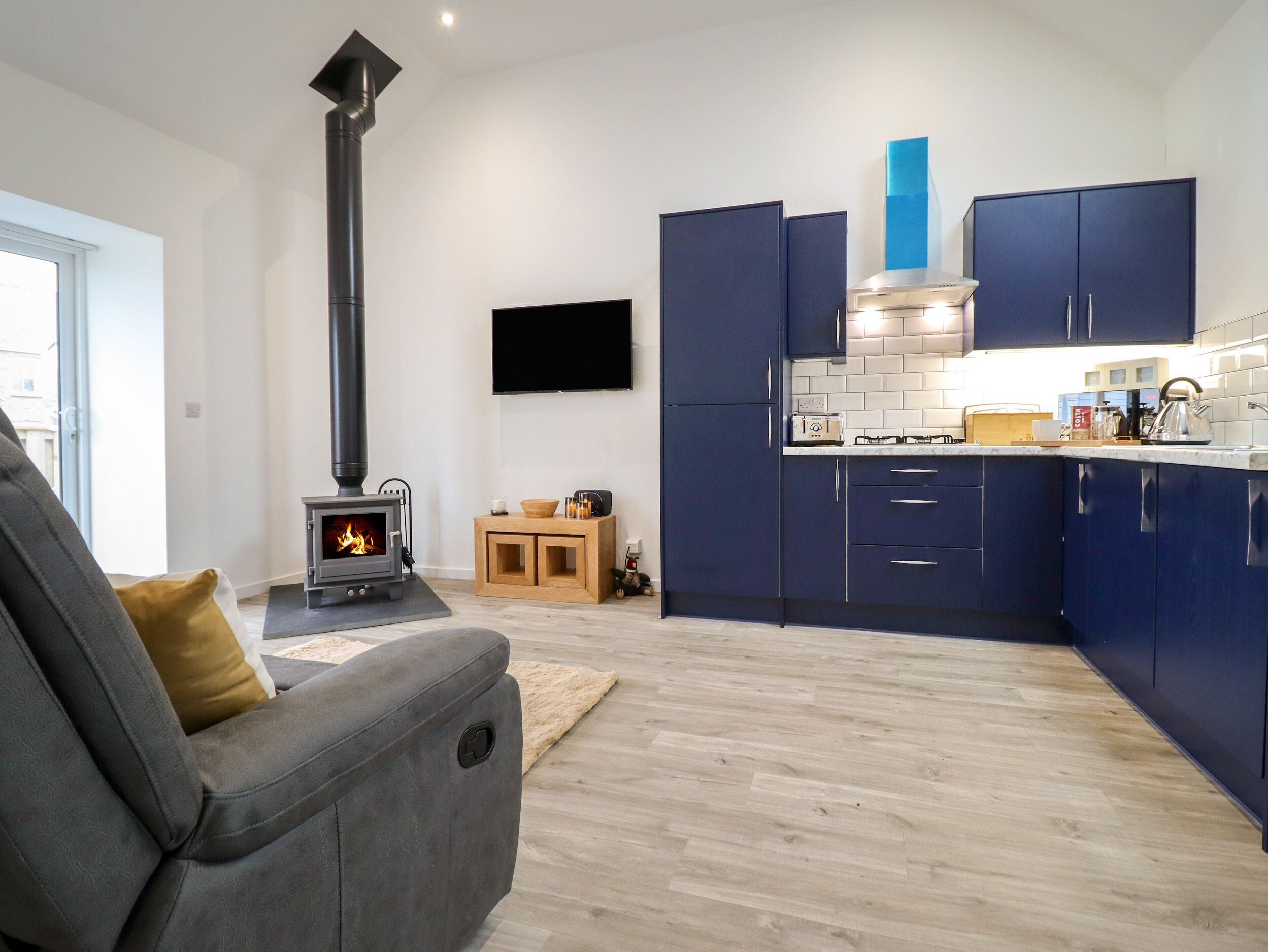 A modern kitchen with dark blue cabinets, a built-in stove, and a flat-screen TV mounted on the wall.