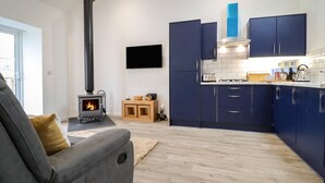 Eine moderne Küche mit dunkelblauen Schränken, einem eingebauten Herd und einem flachbildfernseher an der Wand.