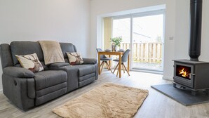 Ein modernes Wohnzimmer mit einem grauen Sofa, einem beigefarbenen Teppich, einem Esstisch mit Stühlen und einem Kaminofen.