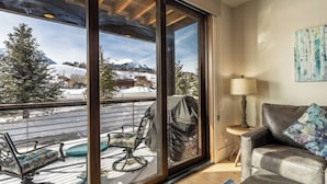 Et værelse med en stor skydedør, der fører ud til en balkon med udendørs møbler og udsigt over sneklædte bjerge.