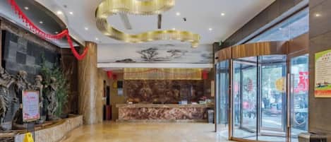 A hotel lobby with a reception desk, a glass entrance, and a marble floor.