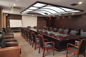 Un salón de conferencias con una larga mesa, sillas, una pantalla de proyector y una pizarra.