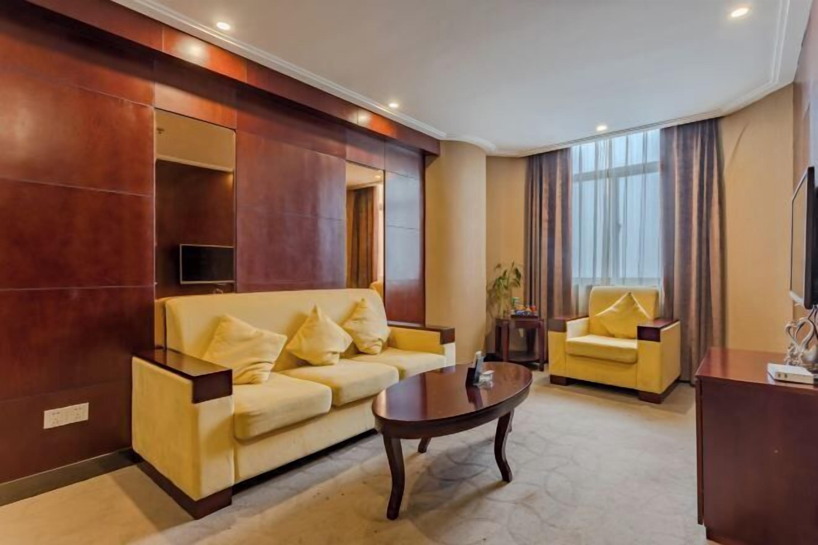 Una sala de estar moderna con sofá, sillón y mesa de centro, un televisor de pantalla plana y un amplio ventanal con cortinas.