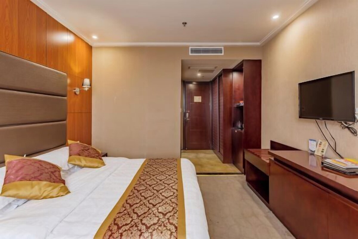 A hotel room with a bed, a desk, a television, and a wardrobe.