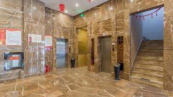 A marble-floored lobby with elevators, a trash bin, and a staircase.
