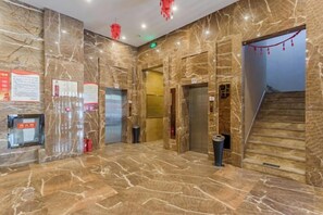 A marble-floored lobby with elevators, a trash bin, and a staircase. - Wancheng Hotel (Qianshan)