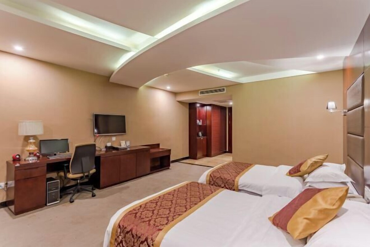 A hotel room with two beds, a desk with a computer, a TV, and a wardrobe.