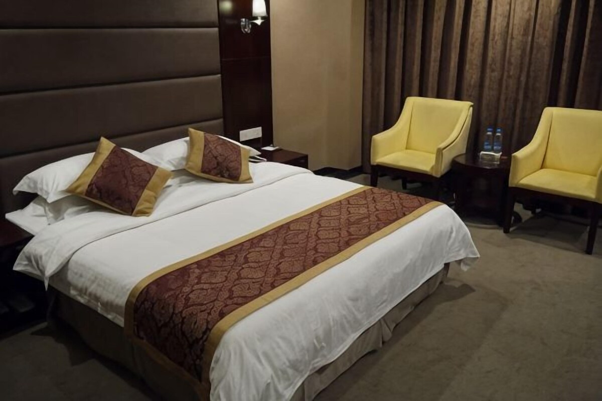 A hotel room with a large bed, two chairs, a nightstand, and a wooden headboard.