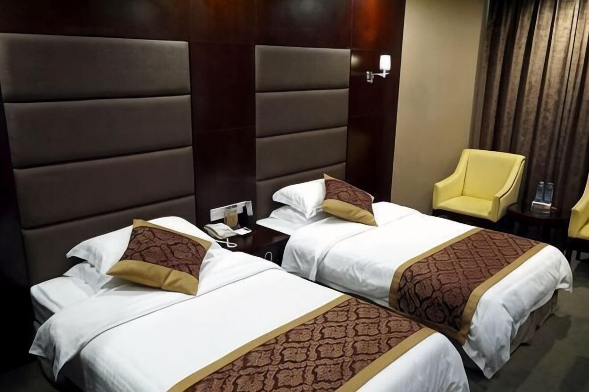 Habitación de hotel con dos camas, una silla y una mesita de noche.