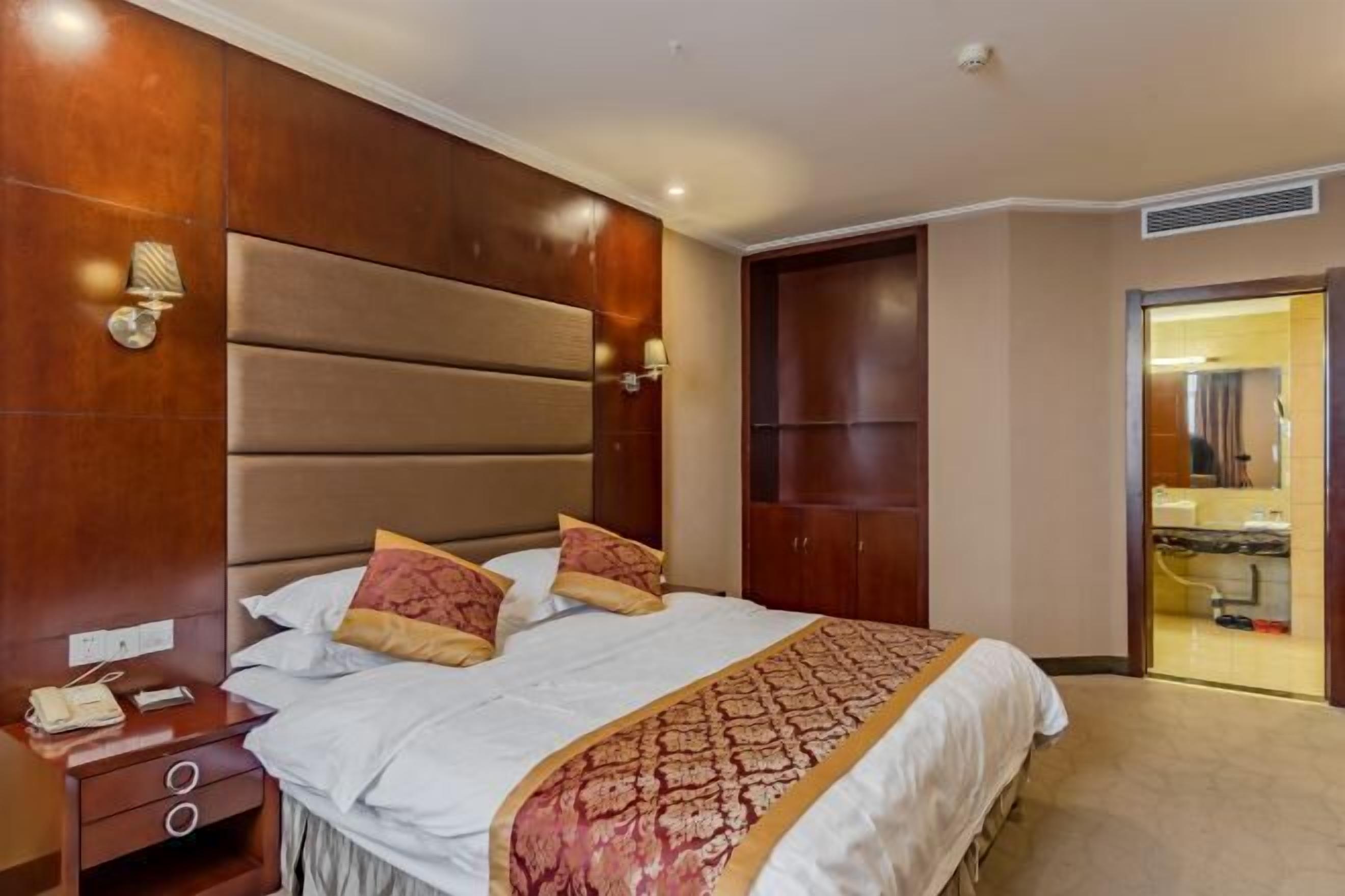 Habitación de hotel con una cama grande, cabecera de madera, mesita de noche con lámpara y un armario.