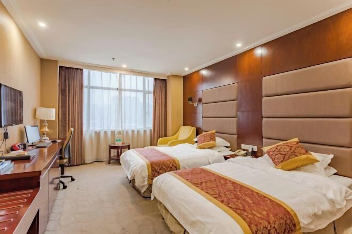 A hotel room with two beds, a desk, a chair, a TV, and a window with curtains.