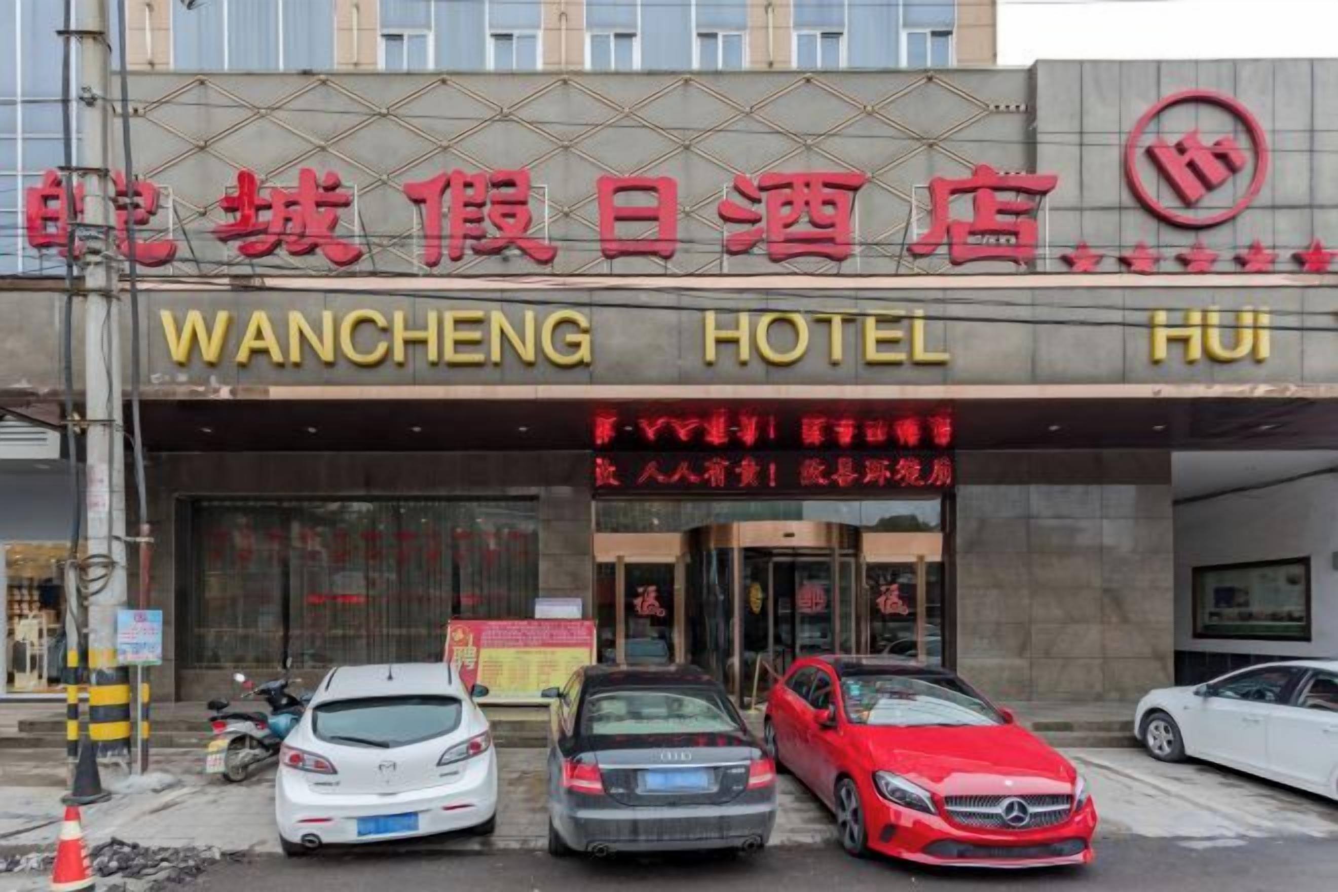 Ingresso di un hotel con una segnaletica in diverse lingue, tra cui l'inglese, e un'area parcheggio con diverse automobili.