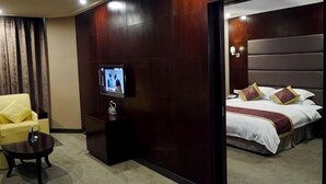 A hotel room with a bed, a television on a stand, a chair, and a small table. - Wancheng Hotel (Qianshan)