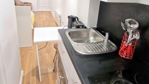 A compact kitchen with a black countertop, stainless steel sink, and a built-in stove. - Cute Studio Apartment in South Croydon (South Croydon)