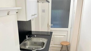 A compact kitchen with a sink, a stove, and a stool. - Cute Studio Apartment in South Croydon (South Croydon)