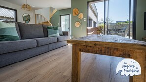 A modern living room with a grey sofa, wooden coffee table, and large windows offering a view of the outdoors. - La Longère de la Plage! Quiet, comfortable villa 300m from the beach! (Trégunc)