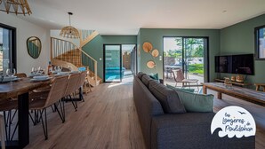 A modern living room with a wooden dining table, a sofa, and a staircase leading to a balcony. - La Longère de la Plage! Quiet, comfortable villa 300m from the beach! (Trégunc)