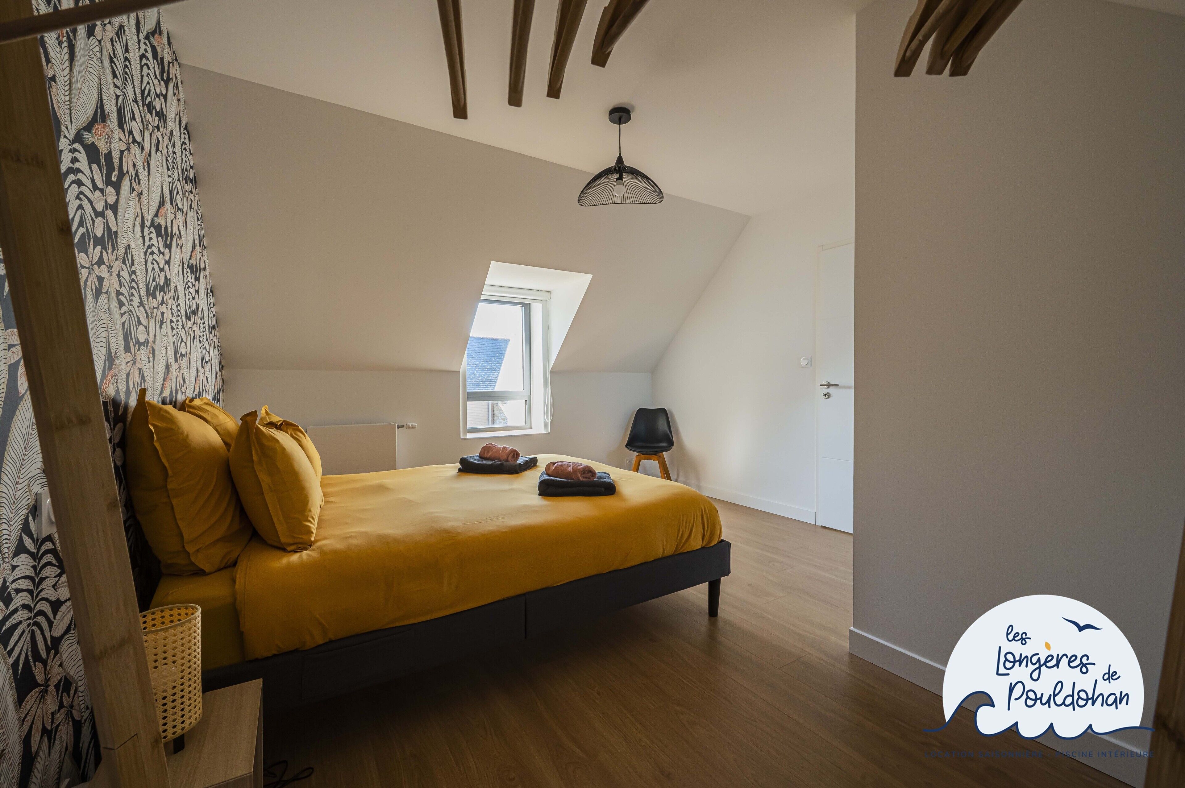 Une chambre à coucher avec un lit, une fenêtre, une chaise et un luminaire suspendu.
