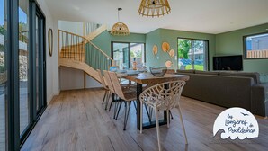 A dining area with a wooden table, wicker chairs, and a staircase leading to another level. - La Longère de la Plage! Quiet, comfortable villa 300m from the beach! (Trégunc)