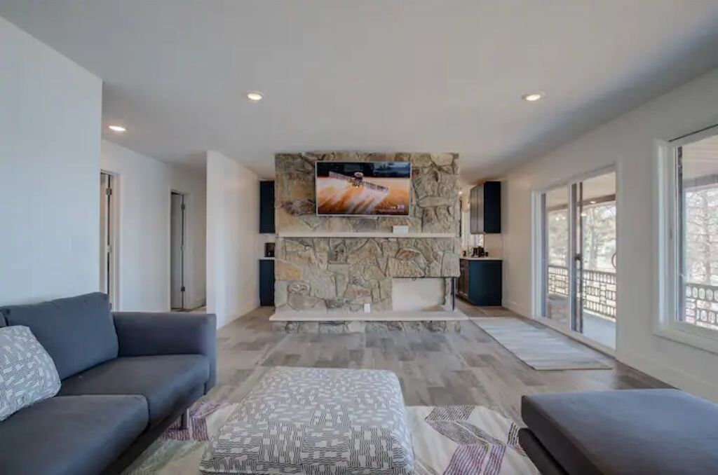 A modern living room with a stone fireplace, a large flat-screen TV, and a grey sofa.