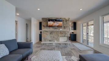 A modern living room with a stone fireplace, a large flat-screen TV, and a grey sofa.