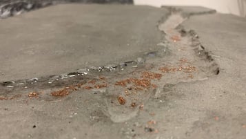 A close-up of a concrete surface with a crack and scattered copper particles.