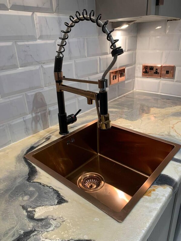 A kitchen with a copper sink, a modern faucet, and a marble countertop.