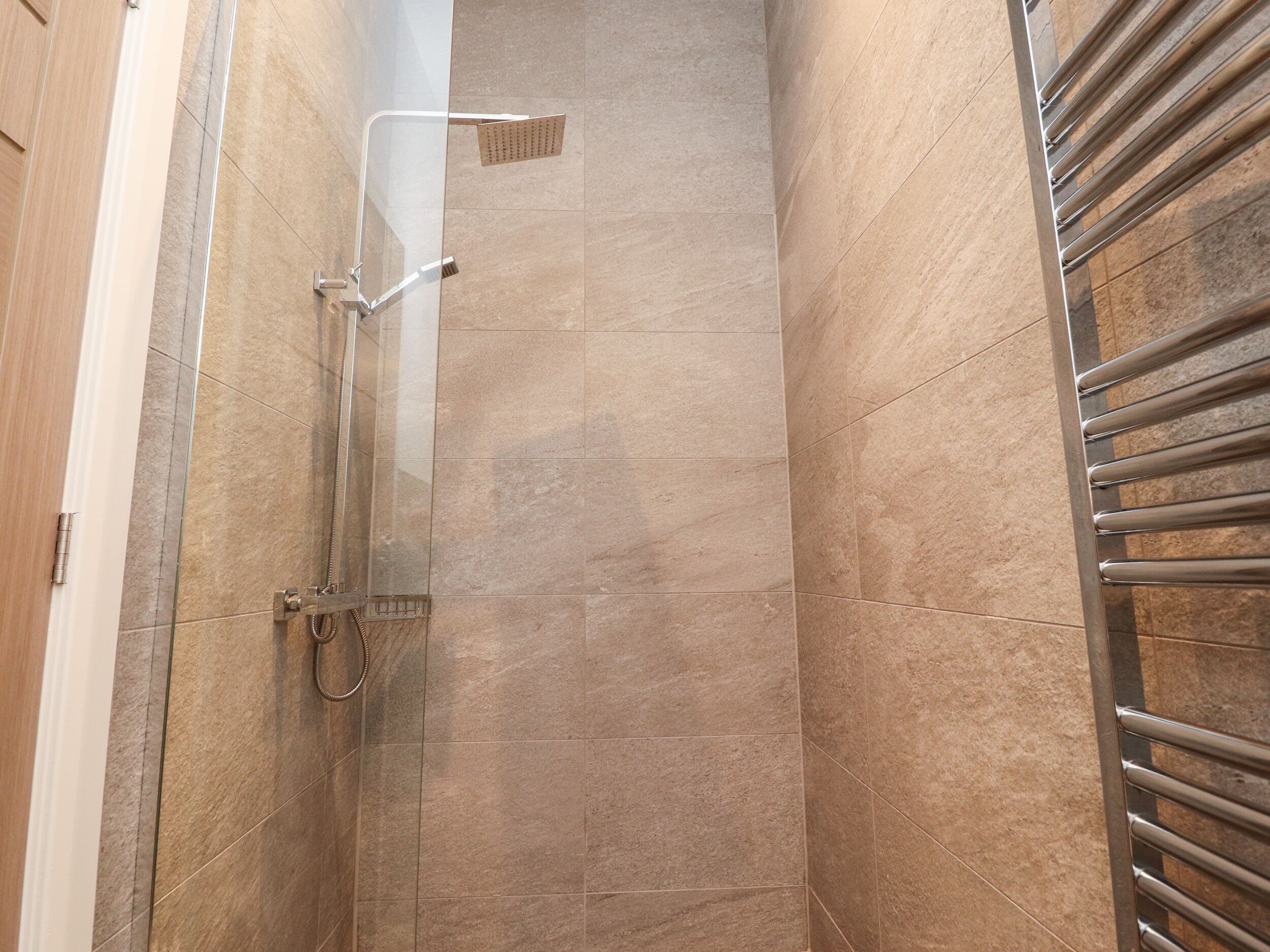 A shower with a glass door, a handheld showerhead, and a wall-mounted control panel.