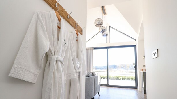 A modern bathroom with white towels hanging on a wooden rack, a grey sofa, and a large window with a view of a snowy landscape. - Skirden View (Clitheroe)