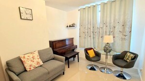 Un soggiorno con un divano grigio, un tavolino, un pianoforte, due poltrone e una lampada.