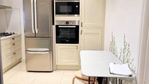 Una cucina compatta con frigorifero, forno e microonde. C'è un tavolo con sedie e un orologio a parete.