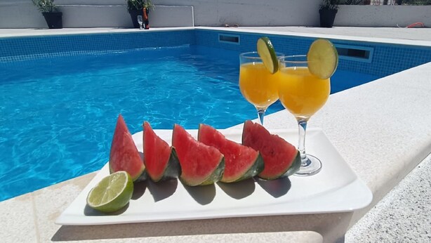 A poolside setting with a white tray holding watermelon slices and a glass of orange juice with lime slices. - Holiday Home Gabi (Bilice)