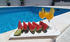 A poolside setting with a white tray holding watermelon slices and a glass of orange juice with lime slices. - Holiday Home Gabi (Bilice)