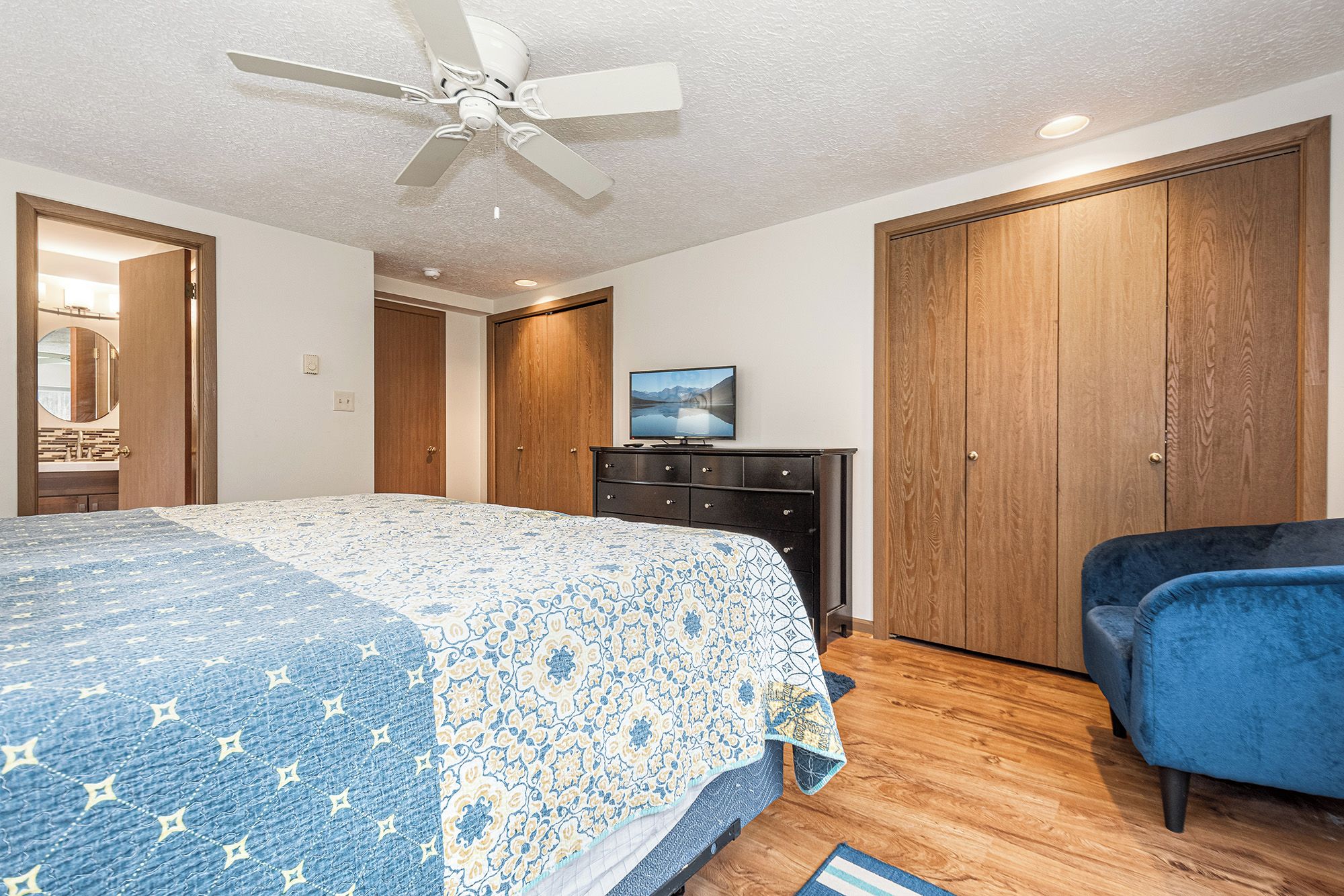A bedroom with a bed, a TV on a dresser, a blue chair, and wooden wardrobes.