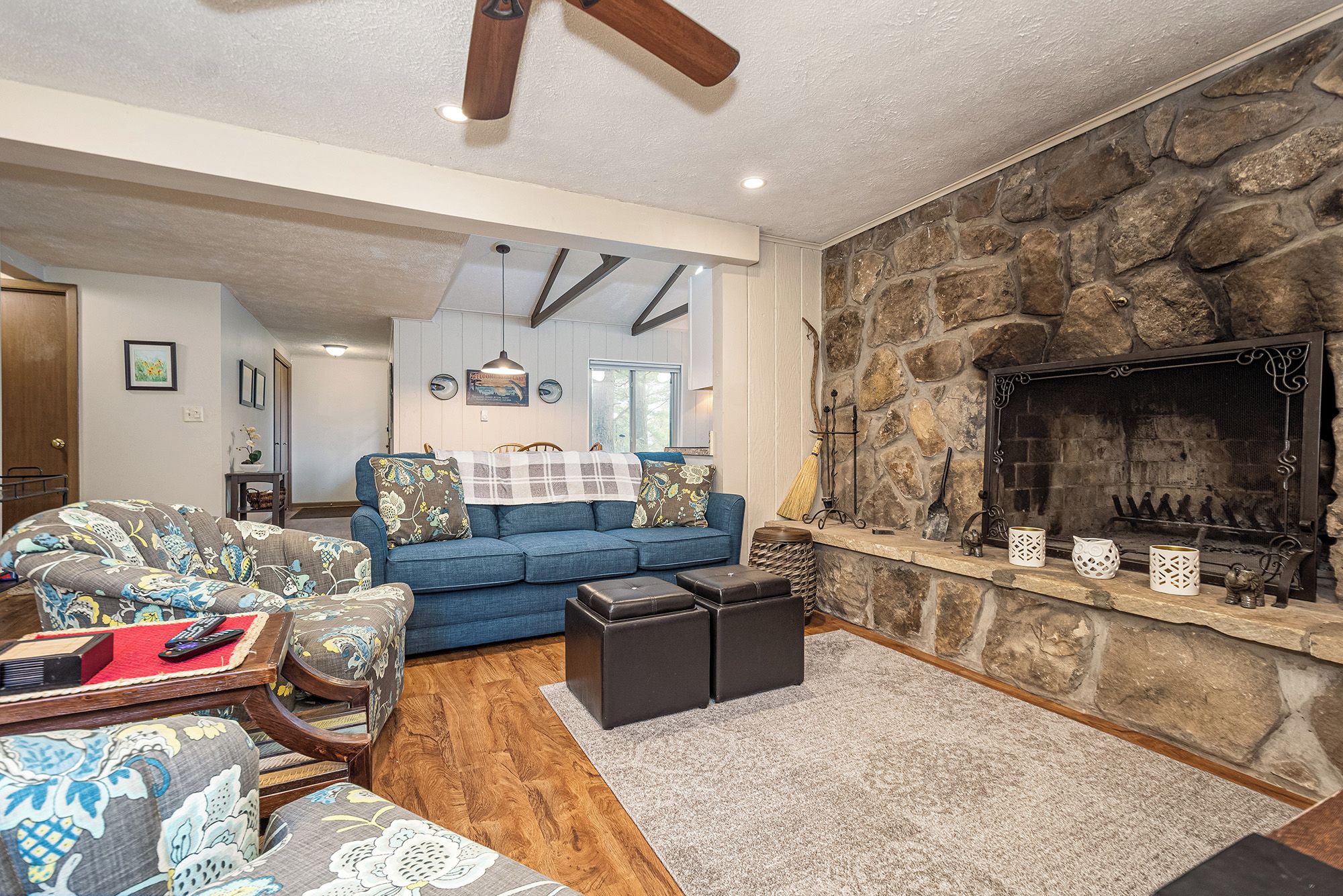 A cozy living room with a stone fireplace, blue sofa, and patterned armchairs.