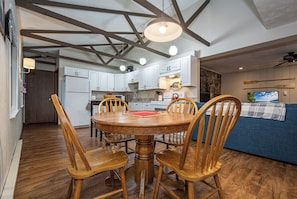 A dining area with a wooden table and chairs, a kitchen with white cabinets, and a stone wall. - Cub House by Taylor Made Deep Creek (McHenry)