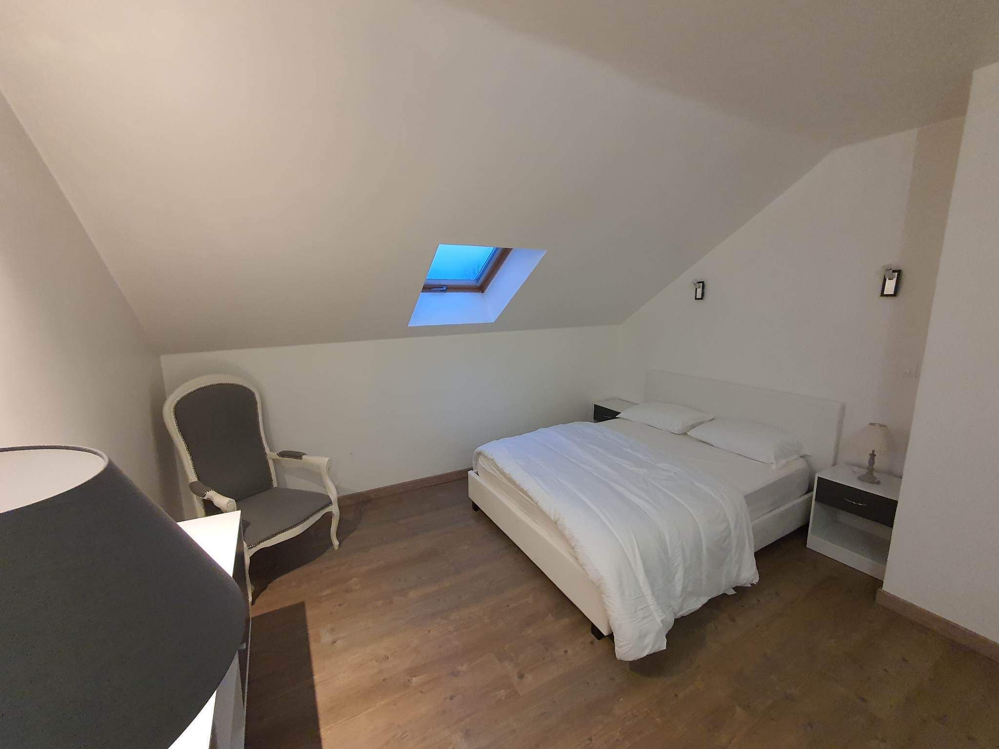 A bedroom with a skylight, a bed, a chair, and a nightstand.