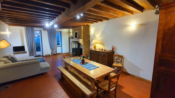 Ein gemütliches Wohnzimmer mit einem Holzesstisch, Bänken und einer Couch. Es gibt einen Kamin, einen an der Wand montierten Fernseher und ein Fenster mit Vorhängen.