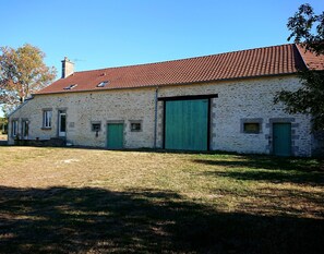 A stone building with a red-tiled roof, green doors, and a large garage door.