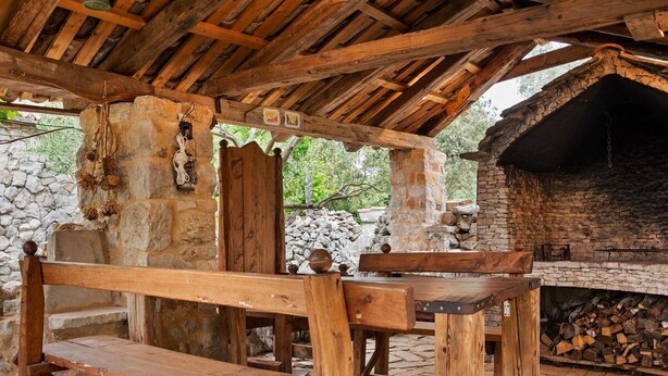 An outdoor wooden structure with a stone wall, a bench, and a fireplace. - Sage House (Trpanj)