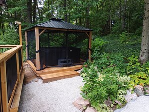 A wooden gazebo with a screened enclosure, surrounded by gravel and greenery. - Waterfront Cottage w/king bed, hot tub, theatre, gym & more (Kawartha Lakes)