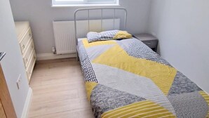 Ein kleines Zimmer mit einem Einzelbett, Fenster, Holzboden und Heizkörper.