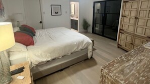 A bedroom with a bed, a nightstand, a lamp, a ceiling fan, a sliding glass door, and a wooden cabinet. - Updated Modern House North Dallas! (Dallas)