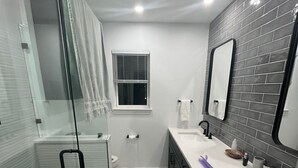 A modern bathroom with a glass shower enclosure, a white sink, a large mirror, and a window. - Updated Modern House North Dallas! (Dallas)