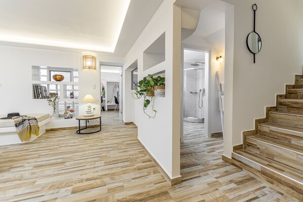 A spacious hallway with wooden flooring, a staircase, and a wall-mounted mirror.