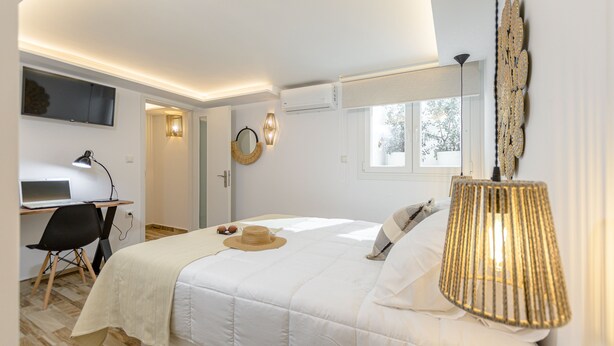 Ett sovrum med en säng, ett skrivbord med en bärbar dator, en stol, en lampa och ett fönster.